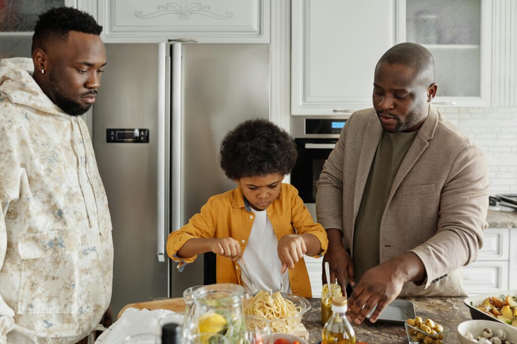 Father and two sons together in the kitchen, with the younger son stirring pasta, demonstrating knife skills, chopping techniques, and food preparation. The family is surrounded by various kitchen tools and ingredients, showcasing the importance of culinary education, knife safety, and cooking techniques for beginners.






