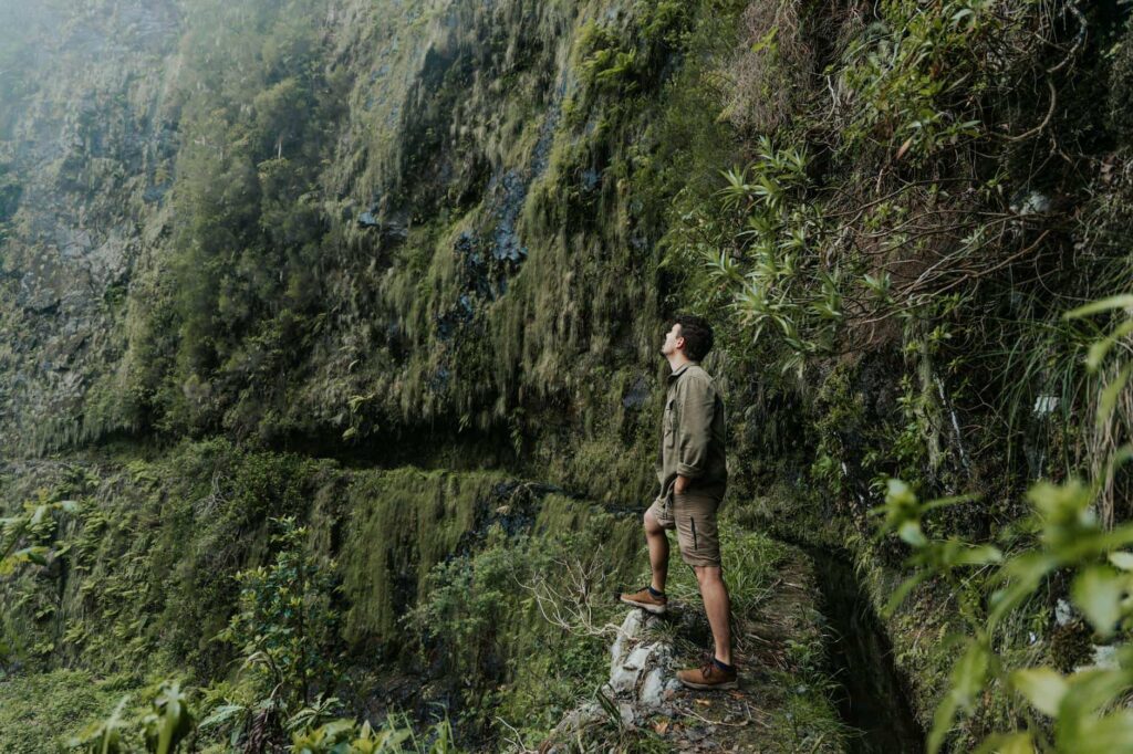 A man in hiking gear stands on a lush, narrow trail, looking up at a steep, moss-covered cliff face. This hidden spot offers a challenging and scenic hike for adventure-loving dads in Mexico.






