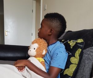 my sick son sitting on the couch with his teddy watching tele