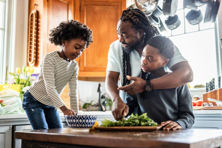 Father cutting vegetables with young children in kitchen